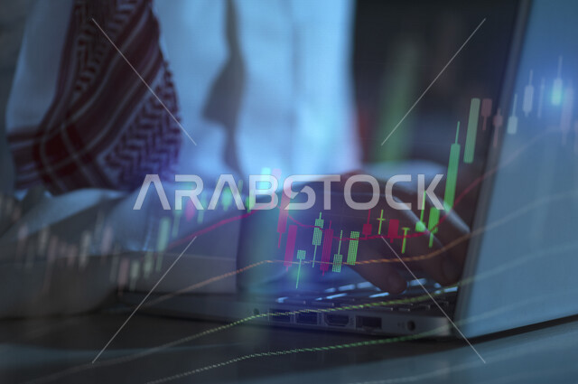 صورة مقربة ليد رجل عربي خليجي سعودي في مقر عمله بالشركة، يتابع البورصة من خلال استخدام الابتوب، رسومات بيانية، صعود ونزول البورصة المالية، الاستثمار المالي والاقتصادي، أعمال الكترونية تجارية