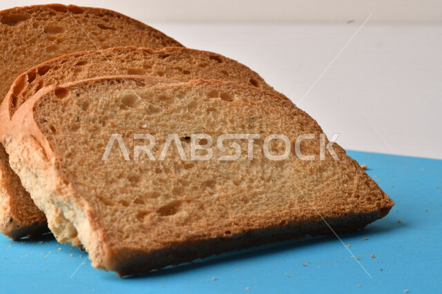 شرائح البقسماط المقرمشة على لوحة التقطيع زرقاء اللون ، صورة مقربة لمخبوزات طازجة محمصة