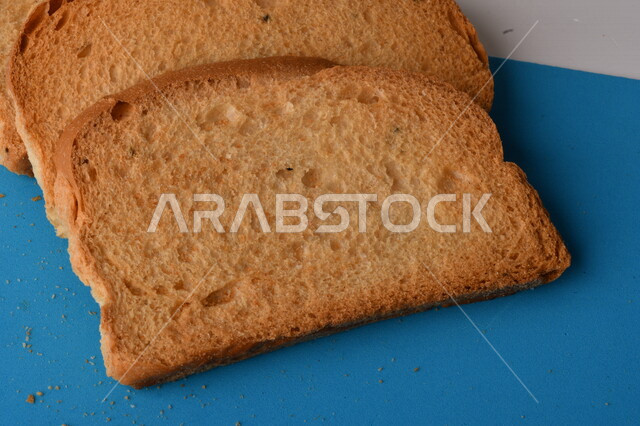 شرائح البقسماط المقرمشة على لوحة التقطيع زرقاء اللون ، صورة مقربة لمخبوزات طازجة محمصة