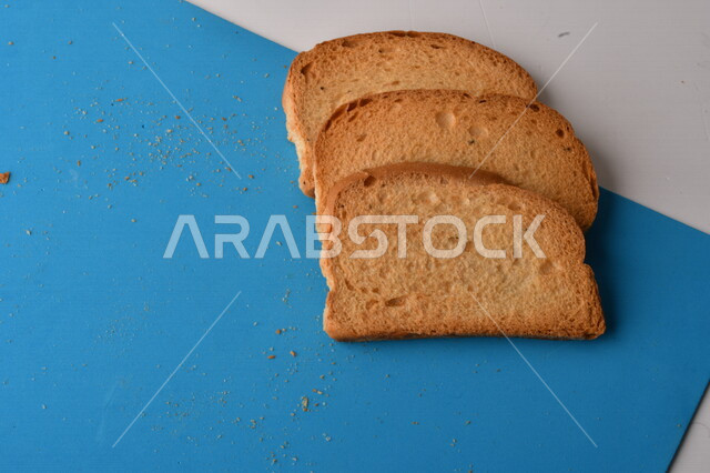 شرائح البقسماط المقرمشة على لوحة التقطيع زرقاء اللون ، صورة مقربة لمخبوزات طازجة محمصة