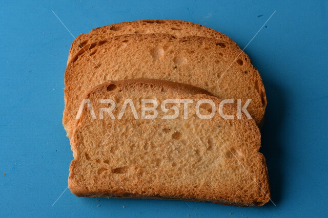 شرائح البقسماط المقرمشة على لوحة التقطيع زرقاء اللون ، صورة مقربة لمخبوزات طازجة محمصة