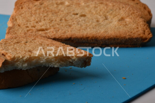 شرائح البقسماط المقرمشة على لوحة التقطيع زرقاء اللون ، صورة مقربة لمخبوزات طازجة محمصة