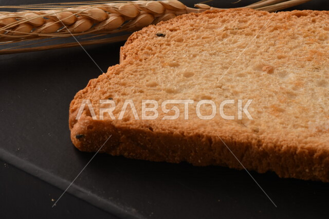 صورة مقربة لمجموعة من نباتات القمح ، وشرائح خبز التوست المحمصة على خلفية سوداء