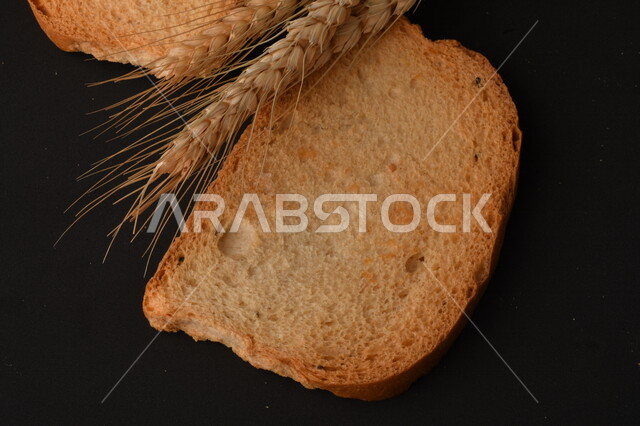 صورة مقربة لمجموعة من نباتات القمح ، وشرائح خبز التوست المحمصة على خلفية سوداء