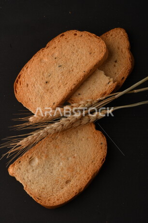 صورة مقربة لمجموعة من نباتات القمح ، وشرائح خبز التوست المحمصة على خلفية سوداء