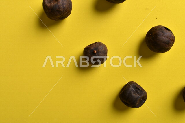 صورة لثمار الجير الأسود المجفف على خلفية صفراء ، الليمون العماني المجفف ، ثمرة الليمون الحامض المجفف ، توابل وبهارات مجففة