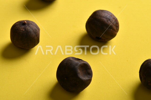 صورة لثمار الجير الأسود المجفف على خلفية صفراء ، الليمون العماني المجفف ، ثمرة الليمون الحامض المجفف ، توابل وبهارات مجففة