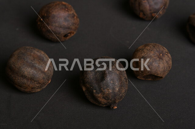 صورة لثمار الجير الأسود المجفف على خلفية سوداء ، الليمون العماني المجفف ، ثمرة الليمون الحامض المجفف ، توابل وبهارات مجففة