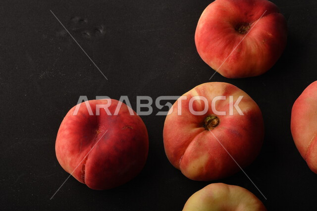 صورة لفاكهة الخوخ المسطح اللذيذ على خلفية سوداء ، ثمرة الدّراق الصحية اللذيذة ، فاكهة الدُّراق المُبلَّط وتسمى كعب الغزال ، فاكهة صيفية