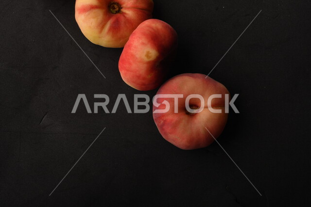 صورة لفاكهة الخوخ المسطح اللذيذ على خلفية سوداء ، ثمرة الدّراق الصحية اللذيذة ، فاكهة الدُّراق المُبلَّط وتسمى كعب الغزال ، فاكهة صيفية