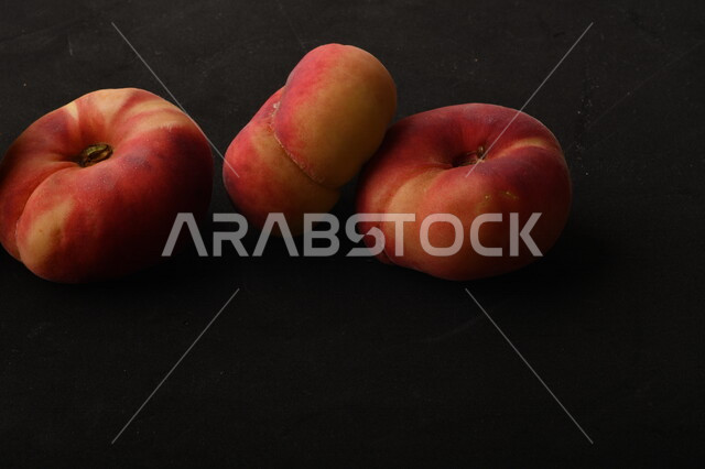 صورة لفاكهة الخوخ المسطح اللذيذ على خلفية سوداء ، ثمرة الدّراق الصحية اللذيذة ، فاكهة الدُّراق المُبلَّط وتسمى كعب الغزال ، فاكهة صيفية