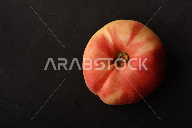 صورة لفاكهة الخوخ المسطح اللذيذ على خلفية سوداء ، ثمرة الدّراق الصحية اللذيذة ، فاكهة الدُّراق المُبلَّط وتسمى كعب الغزال ، فاكهة صيفية