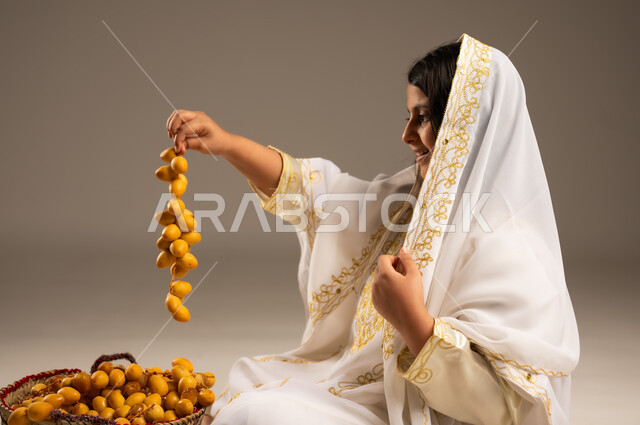 ذكرى تأسيس الدولة السعودية الأولى٢٢فبراير، موسم جني التمور، بورتريه مقرب من الجانب  لفتاة عربية خليجية سعودية ترتدي الشيلة والنشل تمسك بيدها حبات البلح الطازج، يوم بدينا١٧٢٧م، ارتداء أزياء المنطقة الشرقية،  منتجات ومحاصيل زراعية محلية وطنية، خلفية بيج