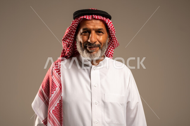 مفهوم الهيبة والوقار، تمثيل الرجولة العربية الأصيلة، بورتريه مقرب لرجل عربي خليجي سعودي كبير السن يرتدي الشماغ والثوب التقليدي ينظر الى الكاميرا بايماءات الفرح السرور، الاهتمام بالأناقة والمظهر الخارجي، خلفية بيج
