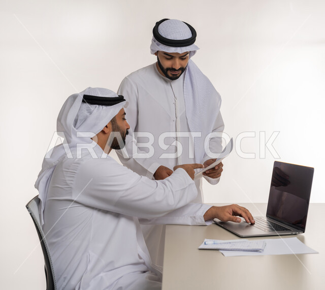 مفهوم الإدارة المتعاونة، بورتريه مقرب من الجانب لموظفين عربيين خليجيين اماراتيين يرتديان الغترة والكندورة البيضاء يناقشان أمور العمل باستخدام الأوراق والبيانات، الوحدة والتفاعل الجماعي لتحقيق أهداف الشركة وحل المشكلات، عقد صفقات شراكة جديدة، خلفية بيضاء
