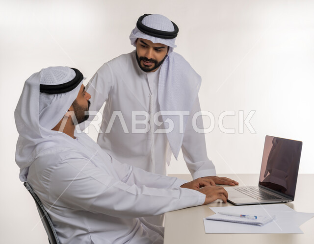 Collaborative management concept, side portrait of two Emirati Gulf Arab employees wearing white ghutra and kandura discussing work matters, unity and team interaction to achieve company goals and solve problems, white background