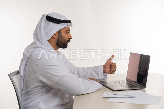 متابعه الأعمال الادارية, تعابير الجودة والرضا والقبول، بورتريه مقرب من الجانب لرجل عربي خليجي اماراتي يرتدي الغترة والكندورة البيضاء ينظر الى الحاسوب بايماءات الثقة بالنفس, تطور التكنولوجيا واستخدام الاجهزة الحديثة لإنجاز المهام, خلفية بيضاء