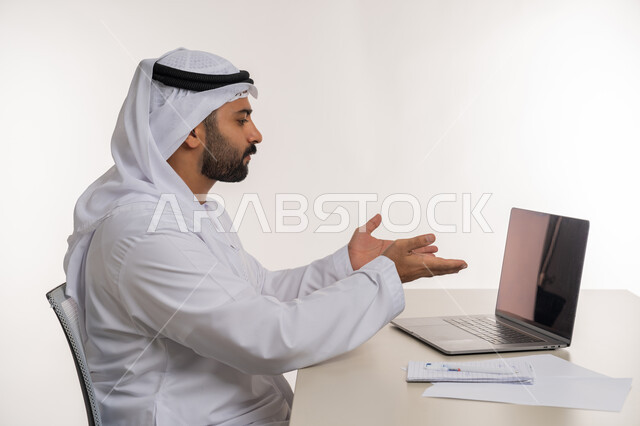 انجاز المهام وتحقيق الاهداف, مهن ووظائف مكتبية, بورتريه لرجل عربي خليجي اماراتي يرتدي الغترة والكندورة البيضاء يشير بكفيه الى شاشة جهاز الحاسوب المحمول بتعابير الاستياء  وعدم الرضا, خلفية بيضاء
