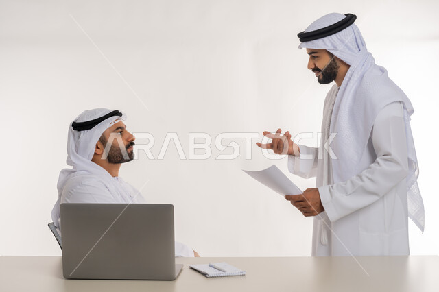 عقد صفقات شراكة جديدة، مفهوم الإدارة المتعاونة، بورتريه مقرب لموظفين عربيين خليجيين اماراتيين مبتسمين يرتديان الغترة والكندورة البيضاء يتناقشان بأمور العمل باستخدام الأوراق والبيانات، الوحدة والتفاعل الجماعي لتحقيق أهداف الشركة وحل المشكلات، خلفية بيضاء