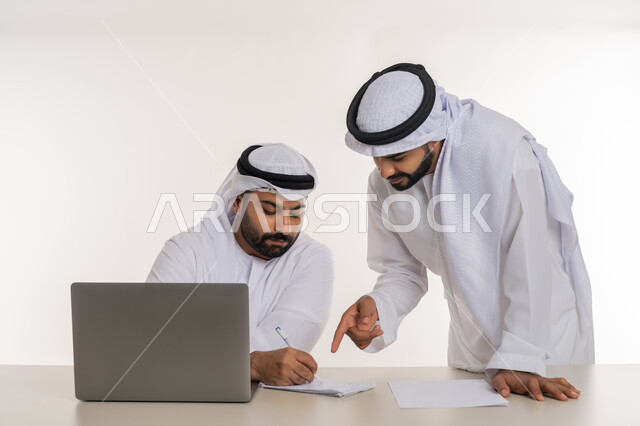 عقد صفقات شراكة جديدة، مفهوم الإدارة المتعاونة، بورتريه مقرب لموظفين عربيين خليجيين اماراتيين مبتسمين يرتديان الغترة والكندورة البيضاء يتناقشان بأمور العمل باستخدام الأوراق والبيانات، الوحدة والتفاعل الجماعي لتحقيق أهداف الشركة وحل المشكلات، خلفية بيضاء