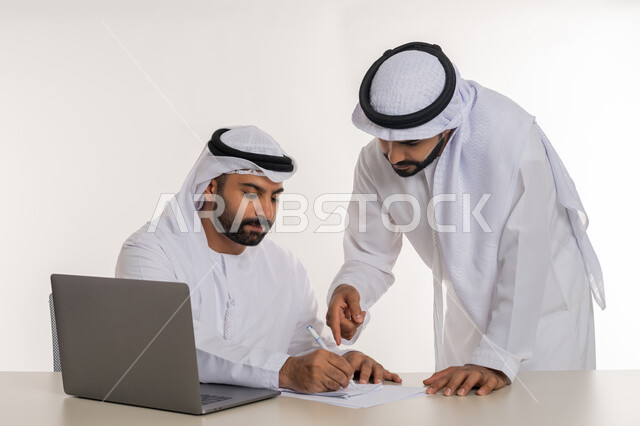 عقد صفقات شراكة جديدة، مفهوم الإدارة المتعاونة، بورتريه مقرب لموظفين عربيين خليجيين اماراتيين مبتسمين يرتديان الغترة والكندورة البيضاء يناقشان أمور العمل باستخدام الأوراق والبيانات، الوحدة والتفاعل الجماعي لتحقيق أهداف الشركة وحل المشكلات، خلفية بيضاء