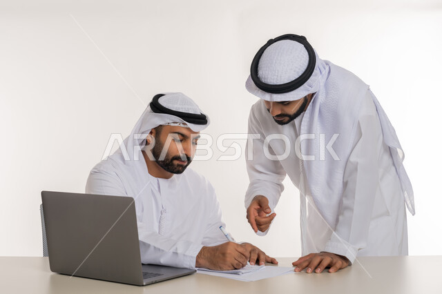 عقد صفقات شراكة جديدة، مفهوم الإدارة المتعاونة، بورتريه مقرب لموظفين عربيين خليجيين اماراتيين مبتسمين يرتديان الغترة والكندورة البيضاء يناقشان أمور العمل باستخدام الأوراق والبيانات، الوحدة والتفاعل الجماعي لتحقيق أهداف الشركة وحل المشكلات، خلفية بيضاء