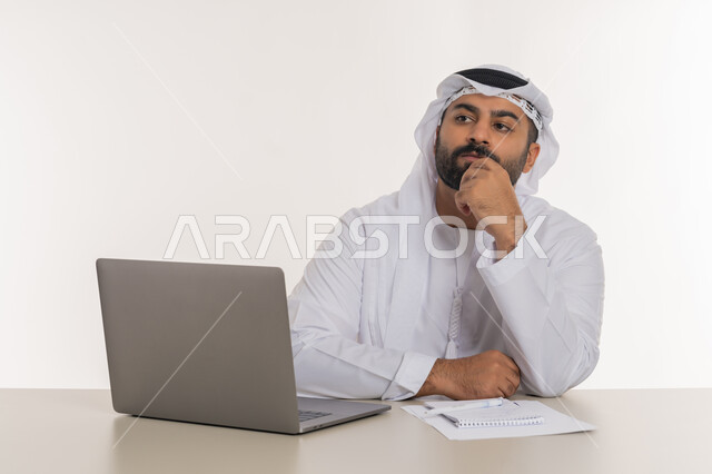تعابير التفكير في استراتيجيات وأهداف العمل، بورتريه مقرب لرجل عربي خليجي اماراتي يرتدي الغترة والكندورة البيضاء  يضع يده على ذقنه ينظر الى شيء ما بايماءات شرود الذهن والحيرة، تطور التكنولوجيا وإستخدام الأجهزة التقنية الحديثة، مهن ووظائف مكتبية, خلفية بيضاء