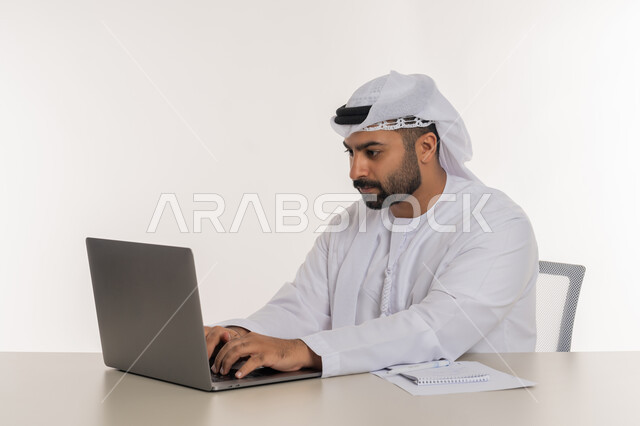 Remote work using laptop in office work, close-up portrait of young Arab Gulf Emirati man wearing white ghutra and kandura looking at laptop with focus gestures, white background