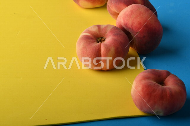 صورة لفاكهة الخوخ المسطح اللذيذ على خلفية ملونة باللونين الأصفر والأزرق ، ثمرة الدّراق الصحية اللذيذة ، فاكهة الدُّراق المُبلَّط وتسمى كعب الغزال ، فاكهة صيفية