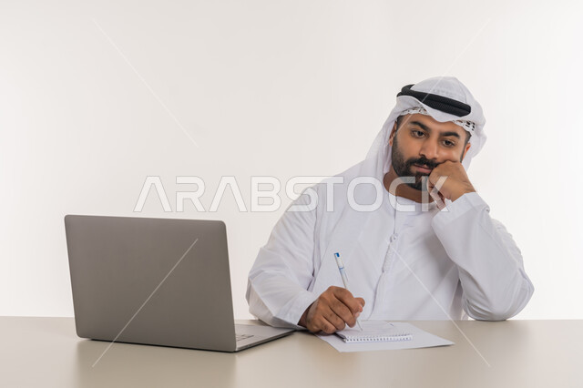 تعابير التفكير في استراتيجيات وأهداف العمل، بورتريه مقرب لرجل عربي خليجي اماراتي يرتدي الغترة والكندورة البيضاء  يضع يده على ذقنه ينظر الى شيء ما بايماءات شرود الذهن والحيرة، تطور التكنولوجيا وإستخدام الأجهزة التقنية الحديثة، مهن ووظائف مكتبية, خلفية بيضاء