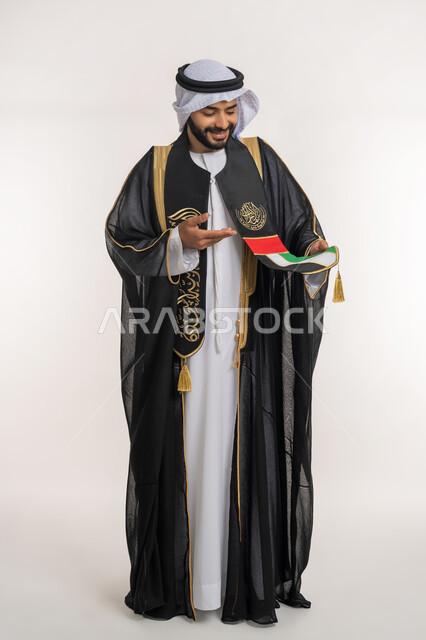 ايماءات  الفخر و الإعجاب، مفهووم حب الوطن والانتماء اليه, اليوم الوطني الاماراتي 2 ديسمبر, بورتريه لرجل عربي خليجي إماراتي يرتدي البشت والوشاح يشير بيده على علم الامارات العربية المتحدة، الجسم بالطول الكامل, خلفية بيضاء