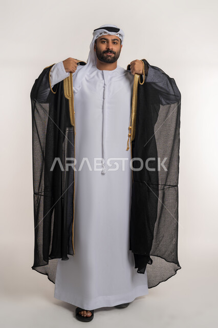 مفهوم الاناقه والاهتمام بالمظهر الخارجي، الوقوف باستقامه والنظر الى الكاميرا بتعابير الثقه بالنفس، بورتريه لرجل عربي خليجي اماراتي يرتدي البشت يقف بايماءات الرجولة، الجسم بالطول الكامل، خلفية بيضاء
