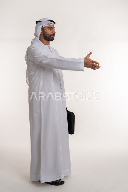 الشعور بالإيجابية والسعادة, الرضا والسرور بالتعارف وتكوين العلاقات الناجحة, مفهوم التحية والسلام, بورتريه لرجل عربي خليجي اماراتي يرتدي الزي التقليدي يقوم بمد كفه للمصافحة، الجسم بالطول الكامل, خلفية بيضاء