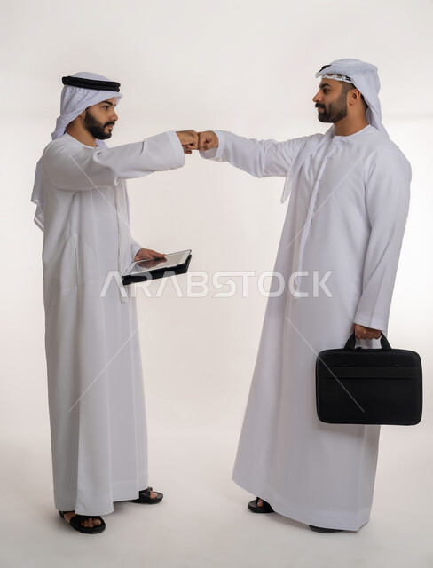 الحفاظ على المسافات بين الاشخاص, بورتريه لرجلين عربيين خليجيين اماراتيين يرتديان الغترة والكندورة يقومان بالتصافح بقبضة اليد، التباعد واتباع احترازات السلامة للوقاية من فايروس كورونا، الجسم بالطول الكامل, خلفية بيضاء