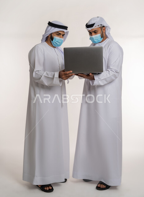 مفهوم الإدارة المتعاونة، بورتريه لموظفين عربيين خليجيين اماراتيين يرتديان الغترة والكندورة والكمامة يتناقشان باستخدام الأوراق، اتباع الاجراءات الوقائية ضد كوفيد19, تحقيق أهداف الشركة وحل المشكلات و عقد صفقات شراكة جديدة، الجسم بالطول الكامل, خلفية بيضاء