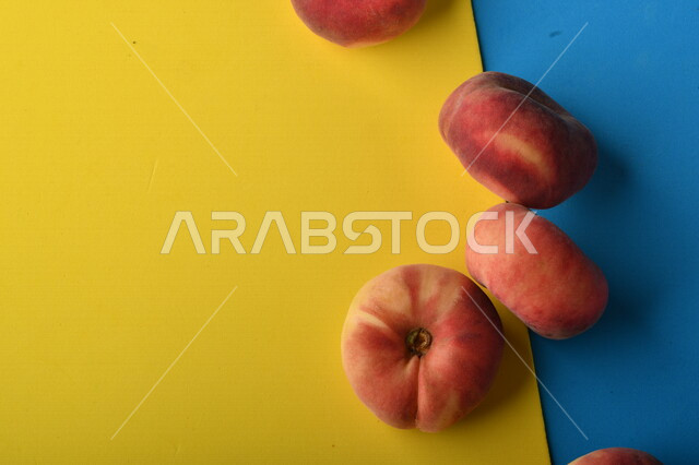 صورة لفاكهة الخوخ المسطح اللذيذ على خلفية ملونة باللونين الأصفر والأزرق ، ثمرة الدّراق الصحية اللذيذة ، فاكهة الدُّراق المُبلَّط وتسمى كعب الغزال ، فاكهة صيفية