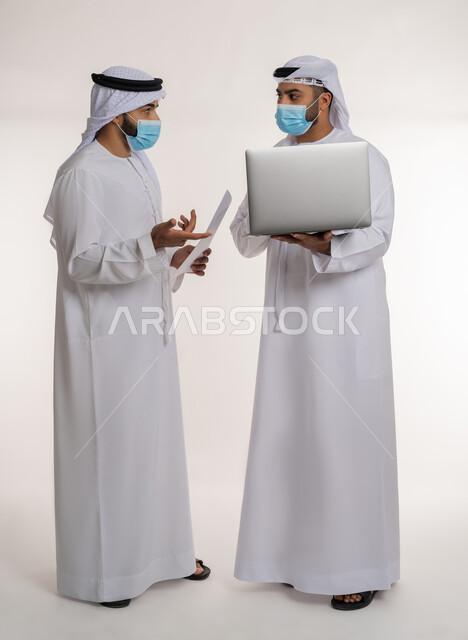 تحقيق أهداف الشركة وحل المشكلات و عقد صفقات شراكة جديدة، مفهوم الإدارة المتعاونة، بورتريه لموظفين عربيين خليجيين اماراتيين يرتديان الغترة والكندورة والكمامة يتناقشان باستخدام الأوراق، اتباع الاجراءات الوقائية ضد كوفيد19, الجسم بالطول الكامل, خلفية بيضاء