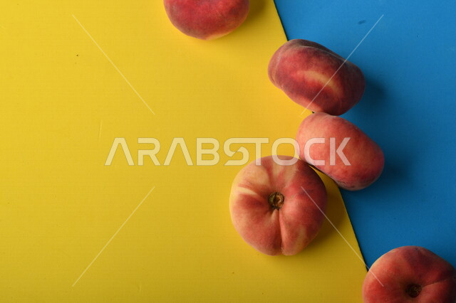 صورة لفاكهة الخوخ المسطح اللذيذ على خلفية ملونة باللونين الأصفر والأزرق ، ثمرة الدّراق الصحية اللذيذة ، فاكهة الدُّراق المُبلَّط وتسمى كعب الغزال ، فاكهة صيفية