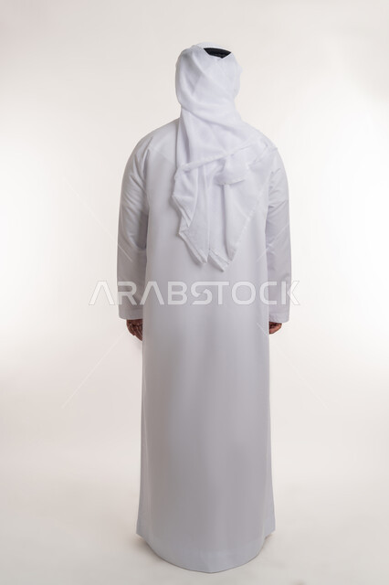 مفهوم الاناقه والاهتمام بالمظهر الخارجي، بورتريه من الخلف لرجل عربي خليجي اماراتي يرتدي الكندوره والغتره البيضاء يقف بايماءات الرجولة، الجسم بالطول الكامل، خلفية بيضاء