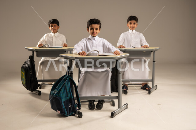 موسم العودة إلى المدارس، بورتريه لمجموعة من الطلاب العربيين الخليجيين السعوديين يرتدون الزي المدرسي يجلسون في مقاعدهم وأمامهم الكتب والمقررات المدرسية، أهداف التربية والتعليم في المملكة العربية السعودية، جودة أساليب التعلم الفعال والمناهج الحديثة، خلفية رمادية