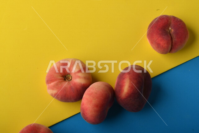 صورة لفاكهة الخوخ المسطح اللذيذ على خلفية ملونة باللونين الأصفر والأزرق ، ثمرة الدّراق الصحية اللذيذة ، فاكهة الدُّراق المُبلَّط وتسمى كعب الغزال ، فاكهة صيفية