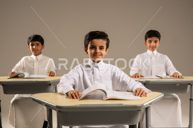 موسم العودة إلى المدارس، بورتريه لمجموعة من الطلاب العربيين الخليجيين السعوديين يرتدون الزي المدرسي يجلسون في مقاعدهم وأمامهم الكتب والمقررات المدرسية، أهداف التربية والتعليم في المملكة العربية السعودية، جودة أساليب التعلم الفعال والمناهج الحديثة، خلفية رمادية