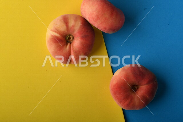 صورة لفاكهة الخوخ المسطح اللذيذ على خلفية ملونة باللونين الأصفر والأزرق ، ثمرة الدّراق الصحية اللذيذة ، فاكهة الدُّراق المُبلَّط وتسمى كعب الغزال ، فاكهة صيفية