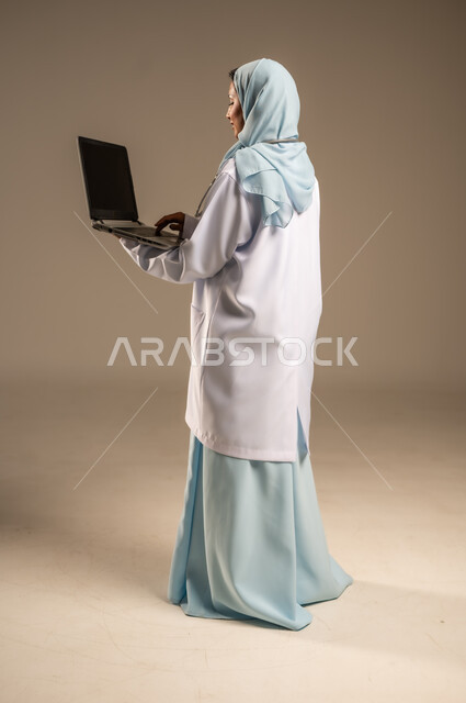 Using technology in research and development, providing services to patients efficiently, conducting medical consultations remotely, portrait of a Saudi Arabian Gulf female doctor wearing a colorful abaya with a white coat working on a laptop, health professions and jobs, colorful background