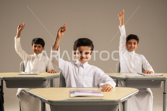 أساليب التعلم الفعال والمشاركة مع المعلم، موسم العودة إلى المدارس، بورتريه لمجموعة من الطلاب العربيين الخليجيين السعوديين يرتدون الزي المدرسي يجلسون في مقاعدهم وأمامهم الكتب والمقررات المدرسية، أهداف التربية والتعليم في المملكة العربية السعودية، خلفية رمادية