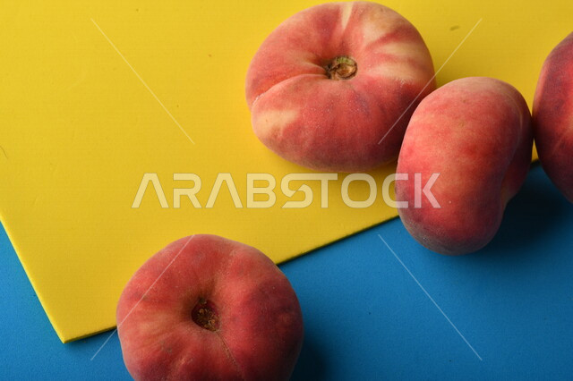 صورة لفاكهة الخوخ المسطح اللذيذ على خلفية ملونة باللونين الأصفر والأزرق ، ثمرة الدّراق الصحية اللذيذة ، فاكهة الدُّراق المُبلَّط وتسمى كعب الغزال ، فاكهة صيفية