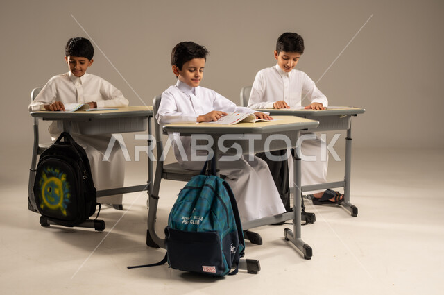 جودة أساليب التعلم الفعال والمناهج الحديثة، موسم العودة إلى المدارس، بورتريه لمجموعة من الطلاب العربيين الخليجيين السعوديين يرتدون الزي المدرسي يجلسون في مقاعدهم وأمامهم الكتب والمقررات المدرسية، أهداف التربية والتعليم في المملكة العربية السعودية، خلفية رمادية