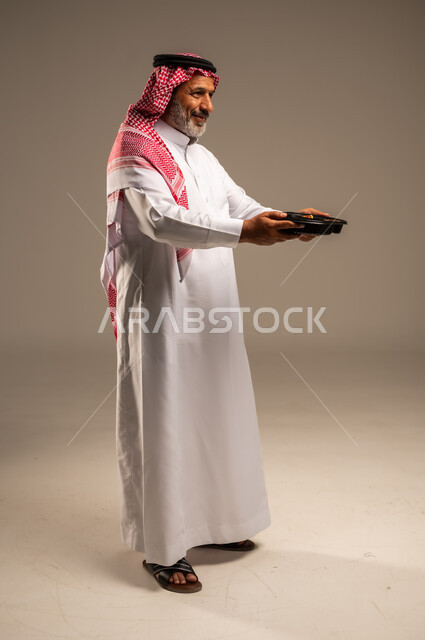 مبادرات وتبرعات انسانية خيرية، الاستمتاع بتناول الوجبات السريعة, بورتريه من الجانب لرجل كبير السن عربي خليجي سعودي مبتسم يرتدي الشماغ والثوب التقليدي يمسك بيده وجبة طعام، توفير الغذاء للمحتاجين، صورة الجسم بالطول الكامل، خلفية بيج