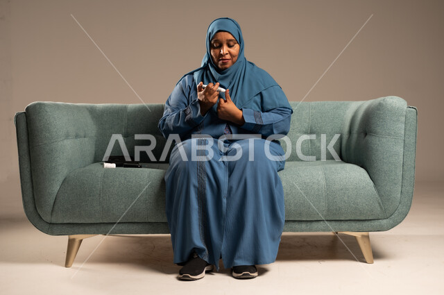 الفحص الطبي السريع في المنزل، أجهزة إلكترونية حديثة ومتطورة لمرضى داء السكري، بورتريه لامراة عربية خليجية سعودية مريضة ترتدي العباءة والحجاب تحمل جهاز قياس سكر الدم تقوم بفحص نسبة السكر في دمها، خلفية بيج