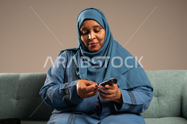 الفحص الطبي السريع في المنزل، أجهزة إلكترونية حديثة ومتطورة لمرضى داء السكري، بورتريه مقرب لامراة عربية خليجية سعودية مريضة ترتدي العباءة والحجاب تحمل جهاز قياس سكر الدم تقوم بفحص نسبة السكر في دمها، خلفية بيج